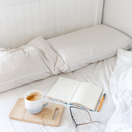 Calm bedroom scene with a journal, pen, coffee mug, and glasses on a neatly made bed, representing realistic self-care and quiet moments for busy women.