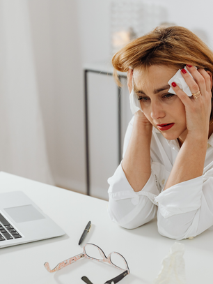 Woman sitting at a desk holding her head while working on a laptop, showing emotional exhaustion and stress from lack of emotional boundaries and work burnout.