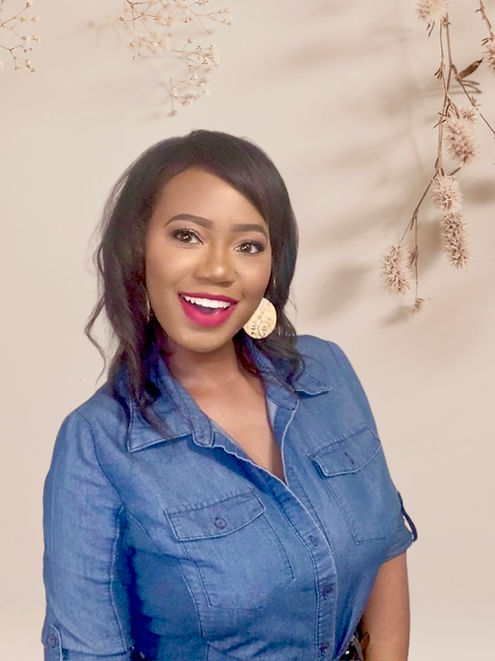 Smiling woman in casual denim outfit with natural floral background | Wellness blogger lifestyle image.