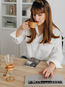 Working mom sitting at a kitchen table with a laptop, drinking coffee and taking a quiet moment to reset before starting her day.
