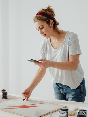 A woman pauses to check her phone while painting at home, a simple moment of social media self-care for single moms.