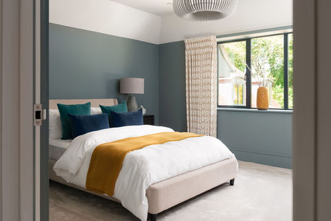 Bedroom with Farrow and Ball De Nimes walls.  Bed styled with white linen and coloured cushion