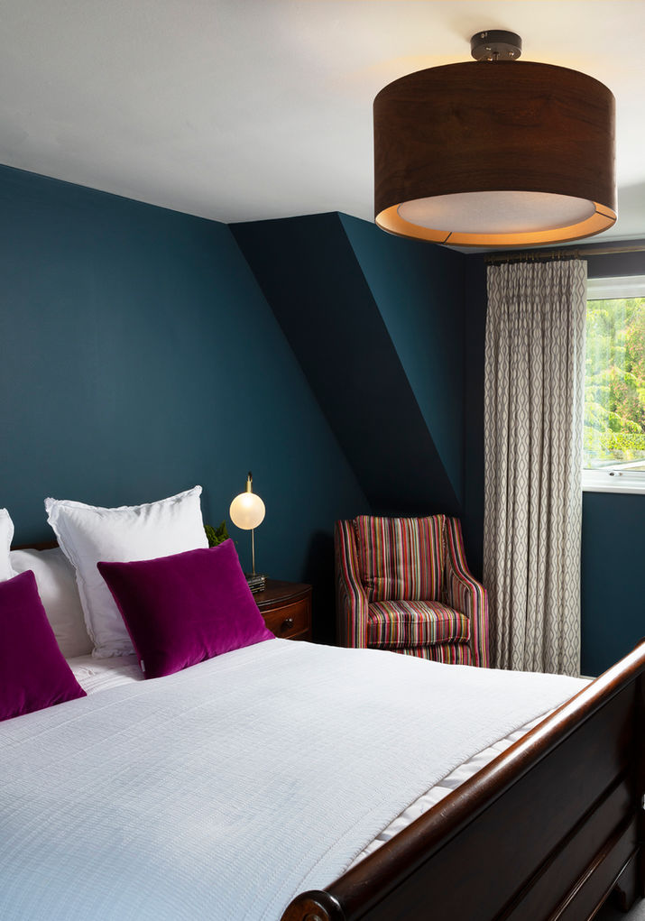 Bedroom styling; crisp white linen with vibrant pink cushions and a toning striped easy chair.