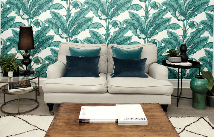 Nature-inspired living room; feature wall in botanical print wallpaper, neutral sofa with teal cushions, wooden coffee table, side table styling.