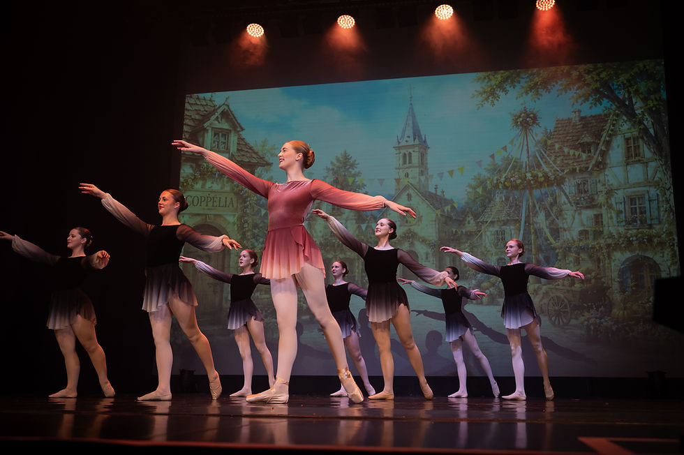 Ballet dancers performing on stage with village backdrop
