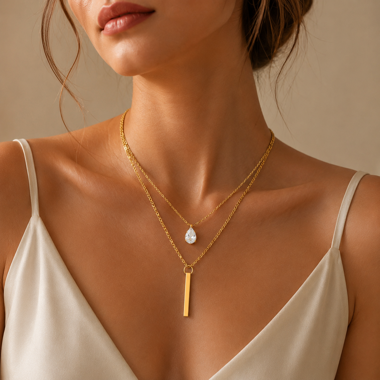 Model wearing layered gold necklace with teardrop crystal and sleek bar pendant in luxury styling