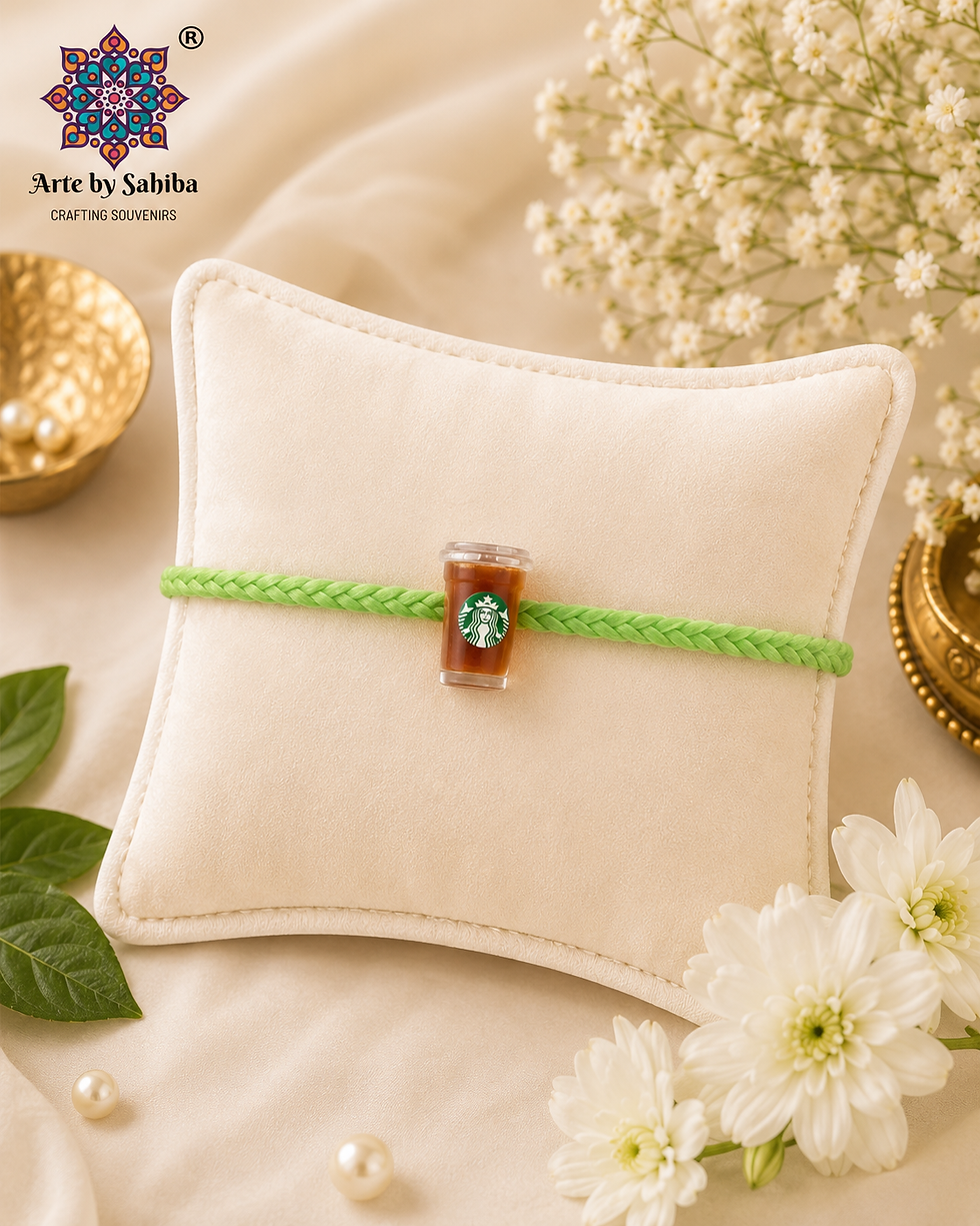 Arte by Sahiba miniature Starbucks iced coffee cup rakhi on a mint green braided thread, displayed on a cream velvet cushion.