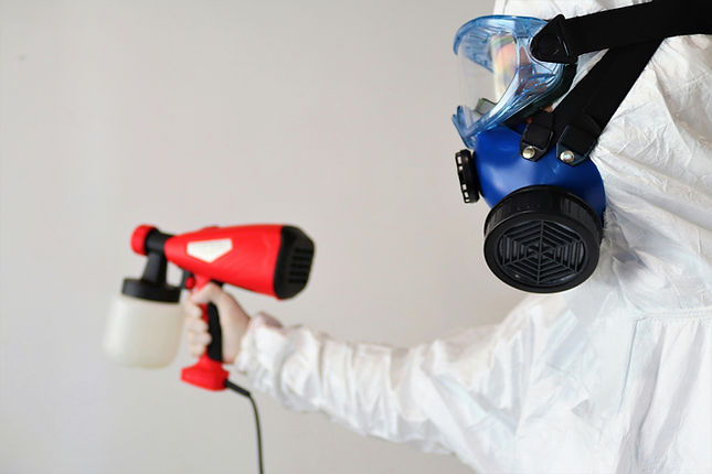 Person in protective suit and respirator holding spray gun