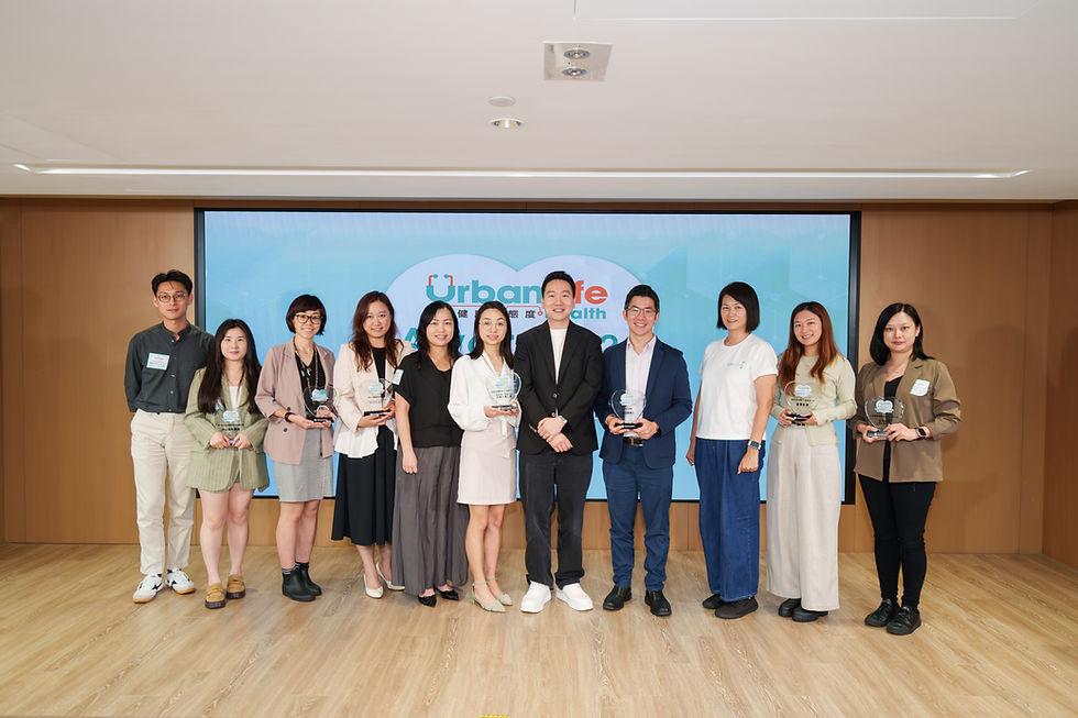 Ten people pose with glass awards in a conference room before a blue UrbanLife health backdrop, smiling.