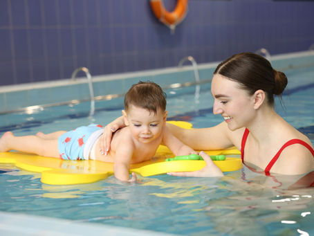 Enfant apprenant progressivement à mettre la tête sous l'eau avec l'accompagnement bienveillant d'un maître-nageur