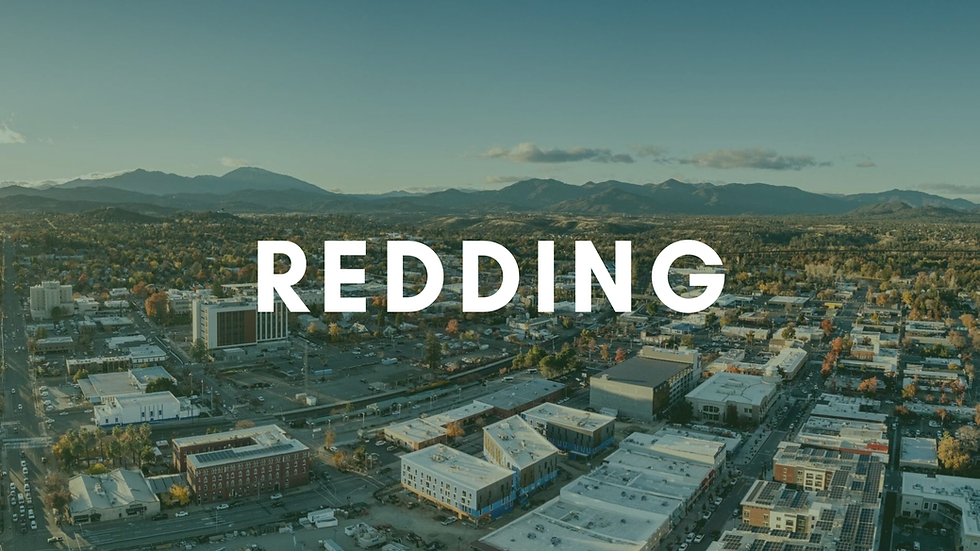 Aerial view of a cityscape with mountains in the background and "REDDING" text over the image. Buildings and roads are visible below.