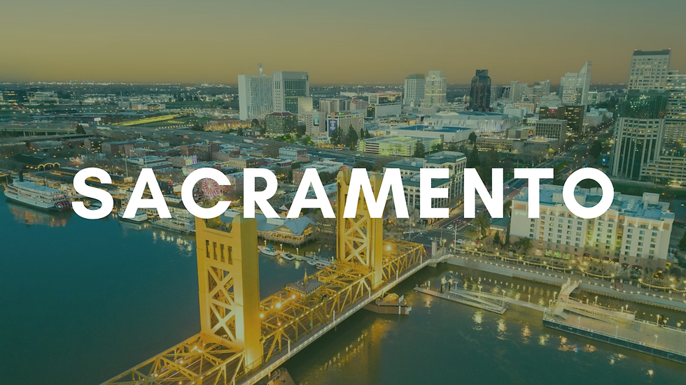 Aerial view of Sacramento skyline at dusk, featuring Tower Bridge over calm river. City lights glow against a soft yellow sky.
