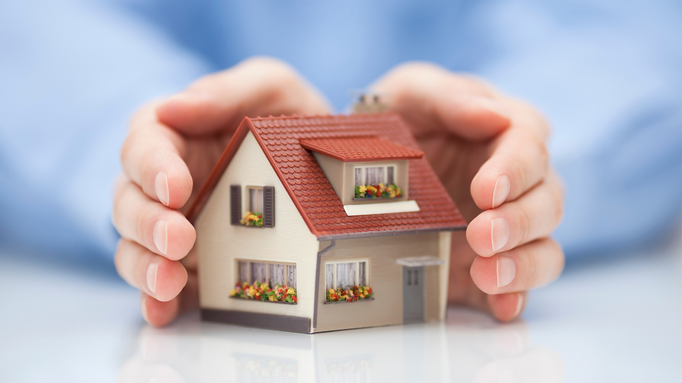 Hands gently cradle a small model house with a red roof and flower boxes, set against a blue background, suggesting protection.