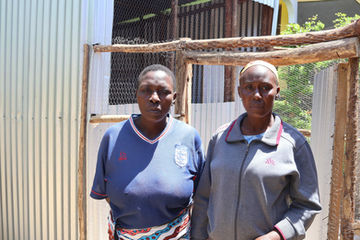 Two single-mother beneficiaries stand beside poultry coops built by Rare Vrienden for community chicken farming.