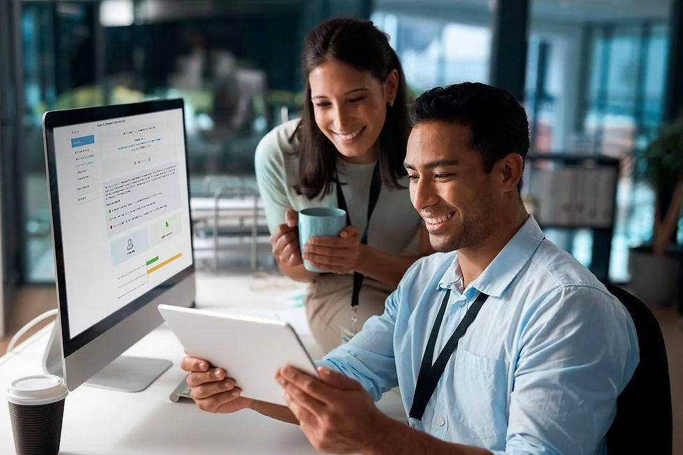 Smiling pair in office. Man holds tablet, woman with mug. Monitor displays document. Modern workspace vibe with bright tones.