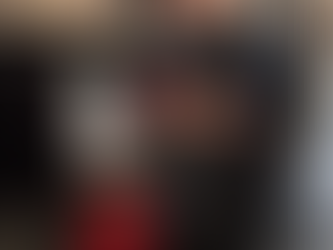 Person in black uniform fixes plumbing under a kitchen sink. Red toolbox nearby. Modern kitchen setting.