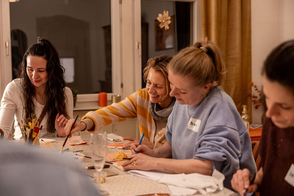 Mehrere Frauen sitzen an einem Tisch und gestalten gemeinsam kreativ mit Stiften, Pinseln und Papier. Sie lachen und arbeiten konzentriert in einer warmen, gemütlichen Atmosphäre beim Soro Community Treffen am 29.01. in Wiesloch.