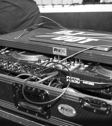 Close-up black and white photo of a professional DJ controller and turntable setup at an event by J Candid Photography.