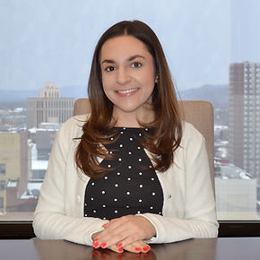 Marisa Maroney sitting in the law firm conference room with the Syracuse skyline visible through the office windows. Photographed by Nicole Morett.