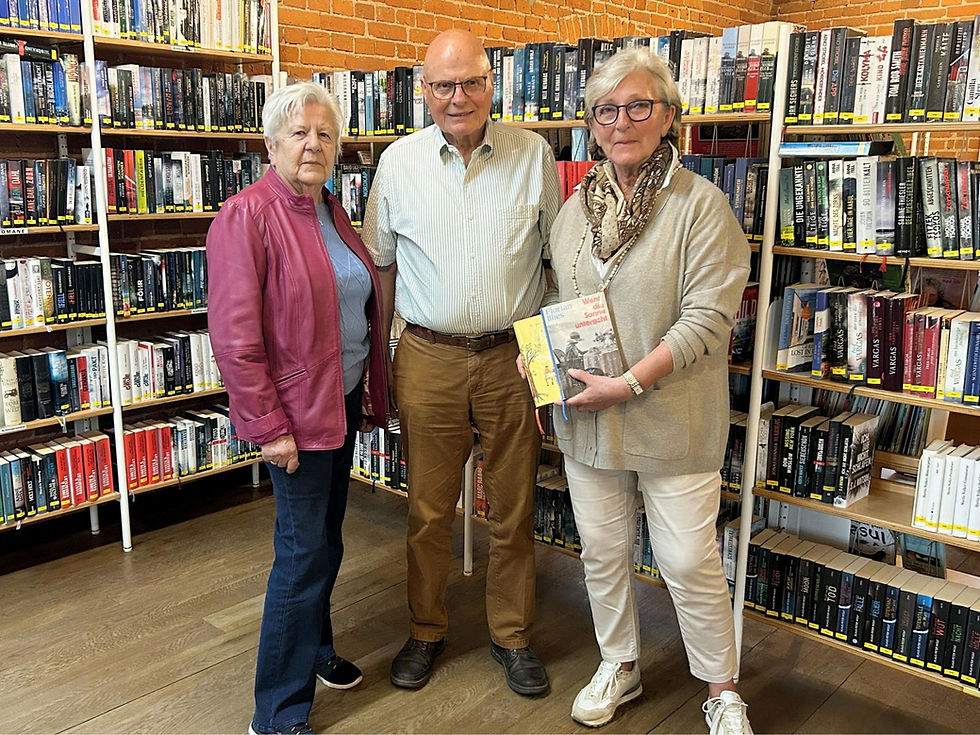 Zwei Seniorinnen und ein Senior vor einem gut gefüllten Bücherregal.