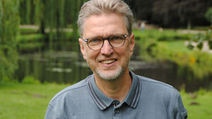 Olaf Schauer in einem Park vor einem Teich mit viel Grün.