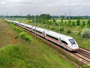ICE-Zug auf einer Bahnstrecke durch viel Grün mit Strommasten.