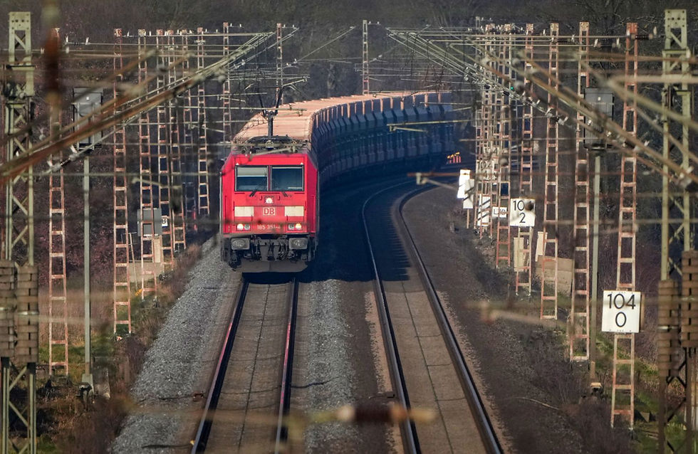 Güterzug auf einer Bahnschiene mit vielen Masten an den Seiten.