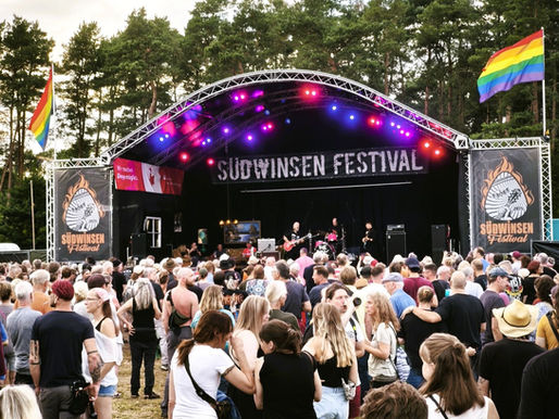 Große Bühne mit Band und Regenbogenflaggen an den Seiten, davor zahlreiche Zuschauer.