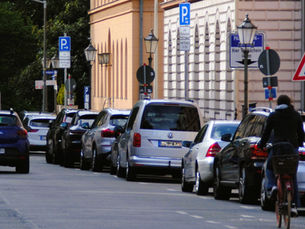 Parkstreifen mit parkenden Autos, Schildern und einer Radfahrerin.