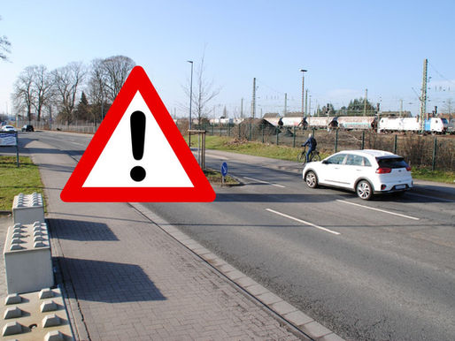 Straße mit Achtungzeichen, Autos und Fahrrad sowie Güterzug im Hintergrund.