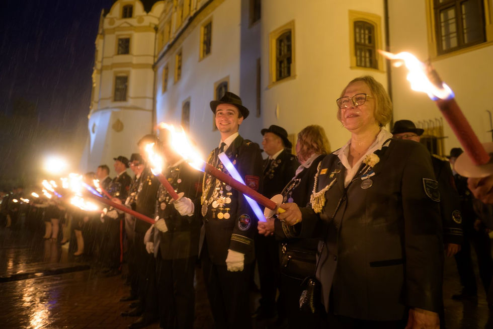Männer und Frauen in Schützenuniformen und Fackeln vor dem Celler Schloss.