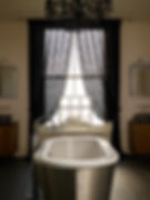 Luxurious bathroom design featuring black damask lace curtains framing period window above freestanding bath, with ornate black chandelier 