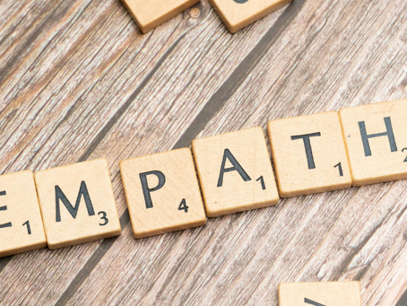 Wooden letter tiles arranged on a wooden surface spell out "EMPATHY," with other scattered tiles showing random letters nearby.