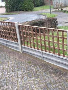 A low wooden fence with lattice panels and concrete posts borders a garden