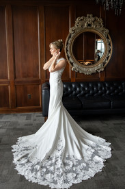 bride fixing earrings looking at ground with lace train at the end of her gown
