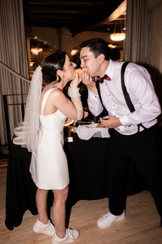 bride in reception dress biting a hot dog with groom 