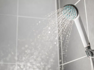 Silver showerhead spraying water against gray tiled wall, creating a refreshing mood.