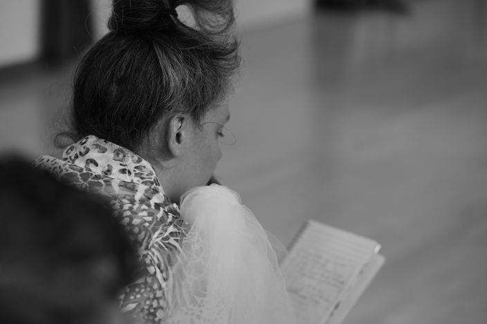 Dancemaker sitting crouched, looking at their notebook.