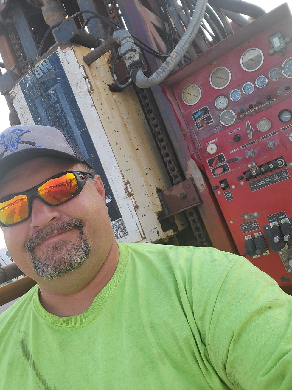 A heavy equipment mechanic in a green shirt smiling in front of heavy machinery