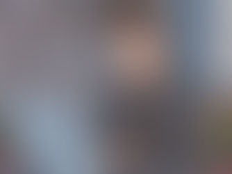 Cartoon man with glasses, wearing a gray shirt and apron, looks worried while typing on a laptop. Books and plants in background.