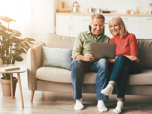 Older couple sitting together on a sofa at home looking at a tablet while reviewing finances and estate planning arrangements.