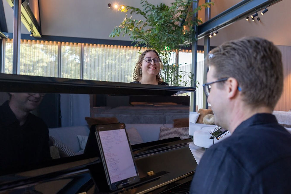 Tim en Maartje bij de piano, warme huiskamersfeer, liggende foto, meerstemmige zang en live muziek.