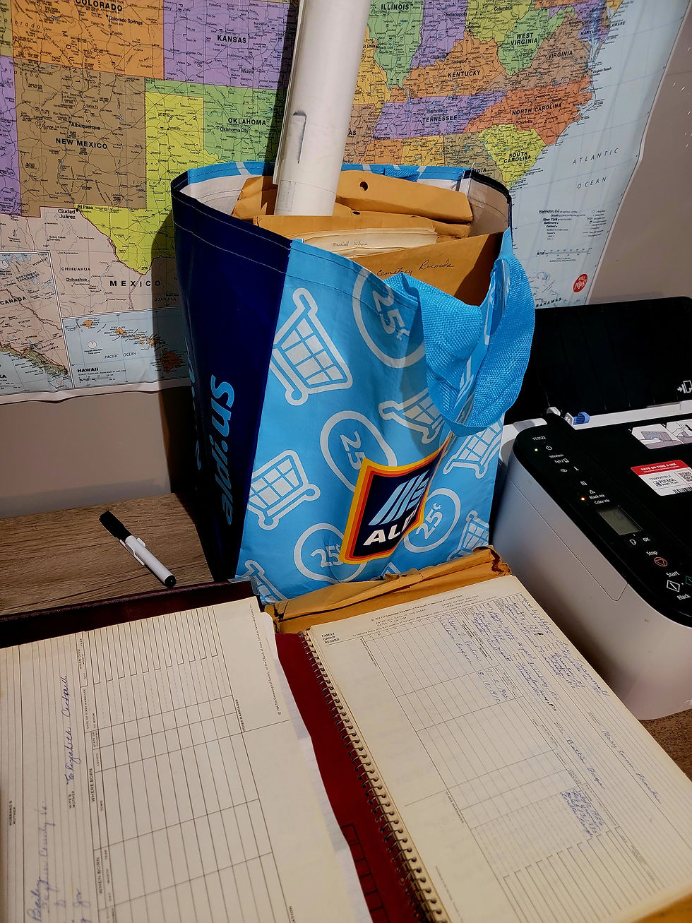 A large Aldi bag is pictured on a desk full of packets of genealogy work. A notebook is opened up in front of the bag displaying censuses.