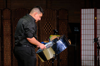 A student dressed in black plays the steel pan on a concert stage