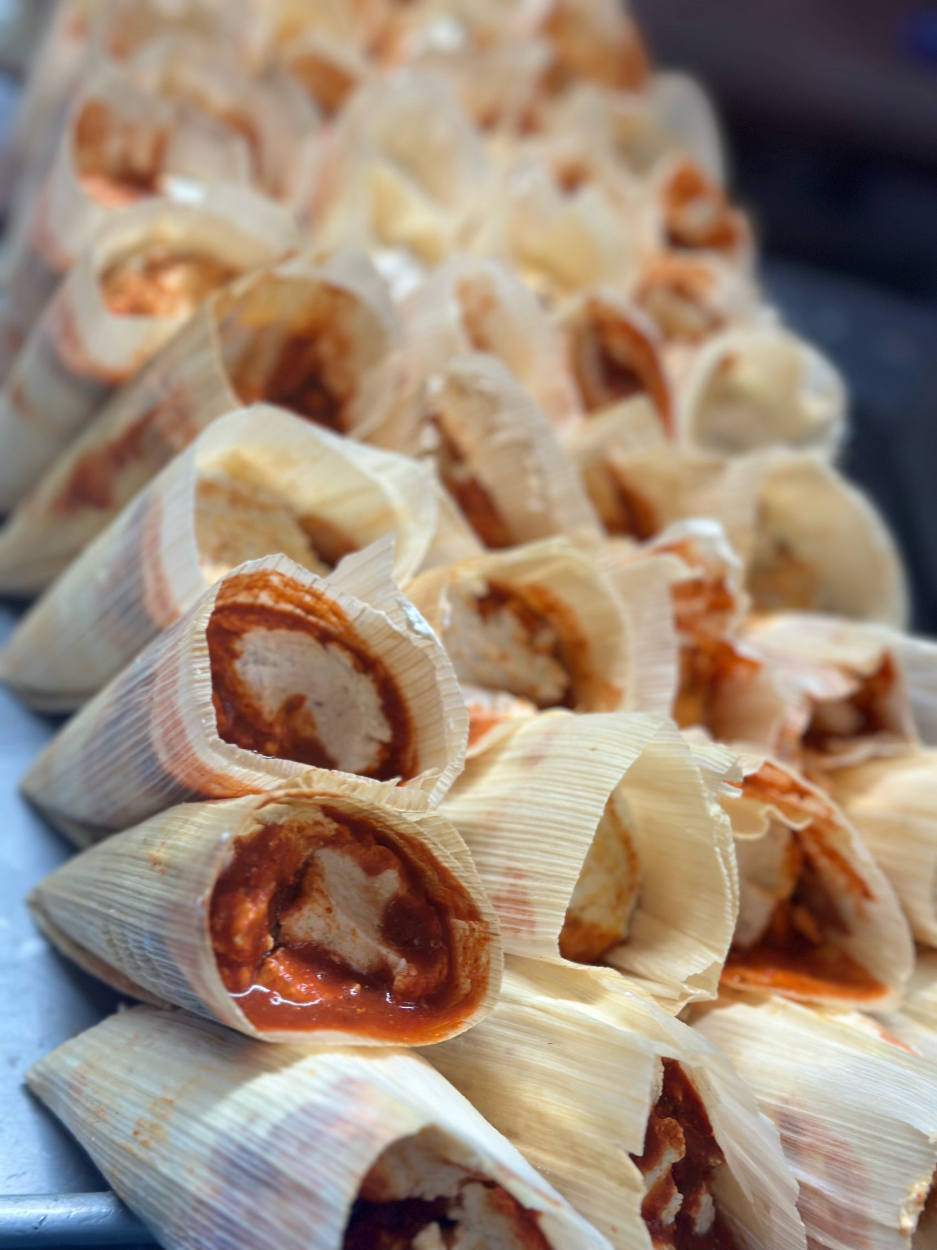Wrapped up tamales with red salsa and chicken ready to cook
