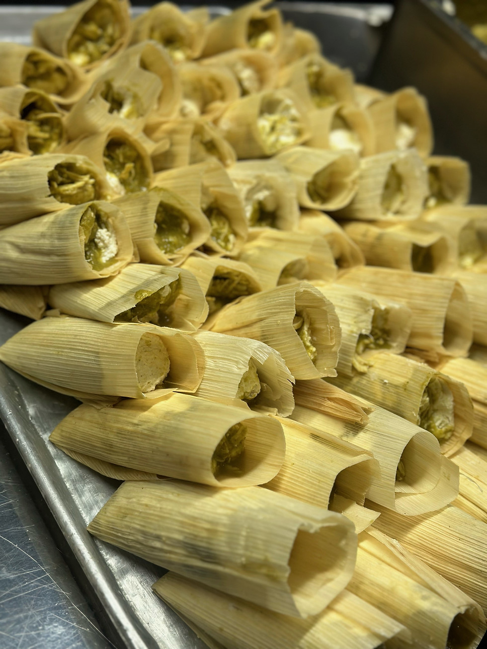 Wrapped up tamales with green salsa and chicken ready to cook