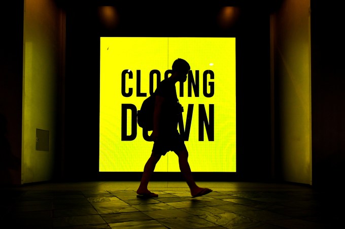 Shadowy figure walking in front of a bright yellow closing down sign with black lettering.