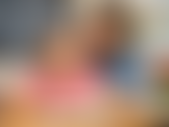 A woman helps a girl read in a classroom. Chalkboard reads "Reading is Fun!" with a map of the USA in the background. Both are smiling.