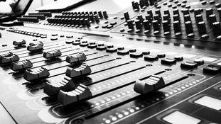 Close-up of a professional audio mixing desk with faders and controls, representing voiceover studio equipment