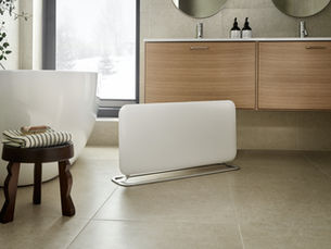 A modern bathroom featuring a sleek, white Mill heater on the floor, offering warmth and style.